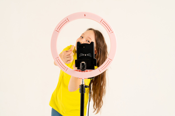 A teenage girl dances and shoots a video. Selfies. The phone is mounted on a tripod and the ring lamp shines. - Photo, Image