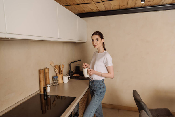 attractive young woman holding cup of coffee in kitchen   - Fotografie, Obrázek