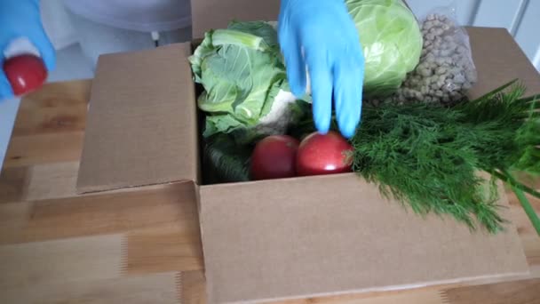 Volunteer in blue gloves holds food donation box vegetables to help others. donation package with foodstuffs. Video footage Full HD - Filmagem, Vídeo