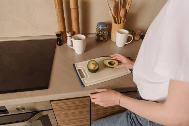 cropped view of woman touching half of tasty avocado near cups  - Foto, Imagem