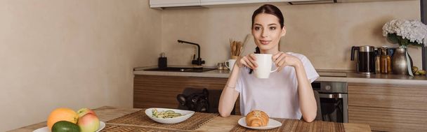 horizontal image of attractive woman holding cup of coffee near tasty breakfast and french bulldog  - Zdjęcie, obraz