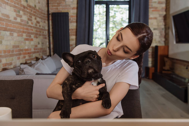 young woman holding in arms and looking at french bulldog  - Foto, imagen
