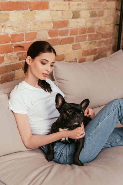 young woman sitting on sofa with black french bulldog  - Photo, Image