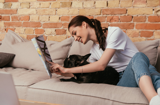 selective focus of happy woman reading magazine near black french bulldog  - Foto, Bild