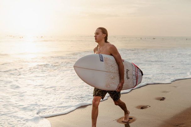 Un uomo sta andando sulla spiaggia con una tavola da surf durante il tramonto, Bali, Canggu
 - Foto, immagini