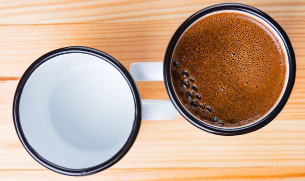 Два металеві старовинні чашки один з кавою, інший порожній на натуральному дерев'яному столі. Плоский вигляд зверху
. - Фото, зображення