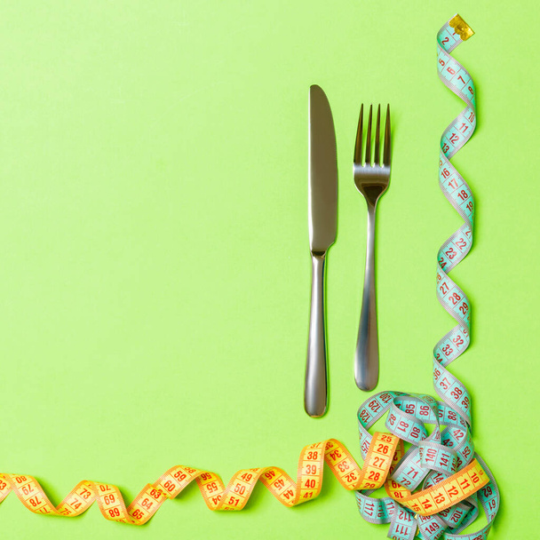 Fork and knife with curled measuring tape on green background with empty space for your design. Top view of proper nutrition concept. - Photo, Image
