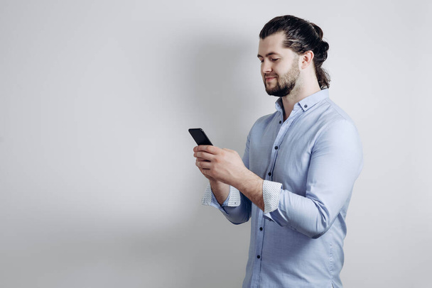 A man in a shirt and with long hair looks at the phone. Gray background - Photo, Image