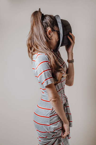 Mooie vrouw in jurk, verbergt haar gezicht met een hoed, Studio shot op op lichte achtergrond - Foto, afbeelding