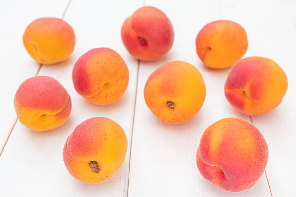 Ripe bright apricots lie on a white wooden surface. Summer fruit harvest. - Photo, Image