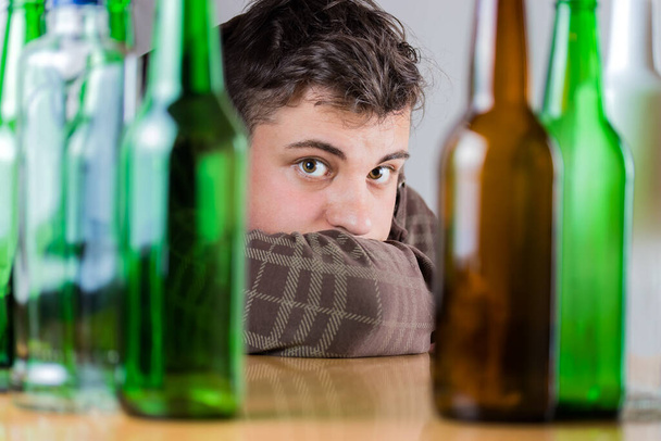 Sad young man behind green and brown glass bottles. Fighting alcohol addiction problem abstract concept. - Photo, Image
