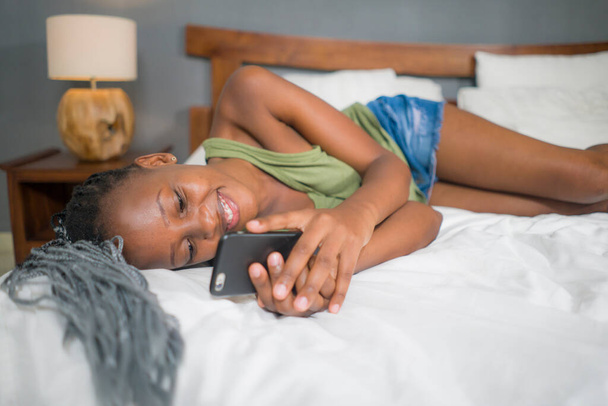 lifestyle home ritratto di giovane donna afro americano felice e attraente nero sdraiato sul letto utilizzando app di social media nel telefono cellulare rilassato e allegro in linea incontri
 - Foto, immagini