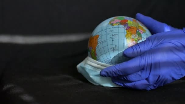 ウクライナのキリル文字で地理的な名前を持つ地球の地球は、保護手袋の医療の手の外科用マスクに身を包んだ上で。世界のコロナウイルス流行 - 映像、動画
