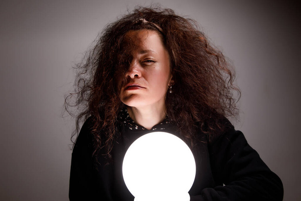 Fortuneteller holding a glowing ball in her hands. Alertness on face - Photo, Image