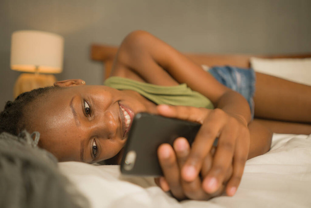 lifestyle home ritratto di giovane donna afro-americana felice e attraente sdraiata sul letto utilizzando l'app di social media nel telefono cellulare rilassato e allegro online incontri
 - Foto, immagini