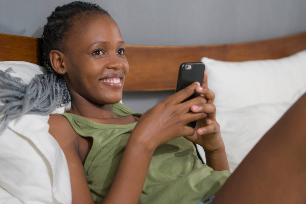 lifestyle home portrait of young happy and attractive black afro American woman lying on bed using social media app in mobile phone relaxed and cheerful online dating - Photo, image