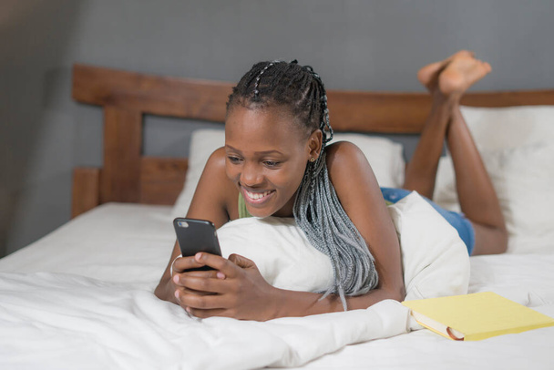 образ жизни портрет молодой счастливой и привлекательной черной афро-американской женщины, лежащей на кровати с помощью приложения социальных сетей в мобильном телефоне расслабленный и веселый онлайн знакомства
 - Фото, изображение
