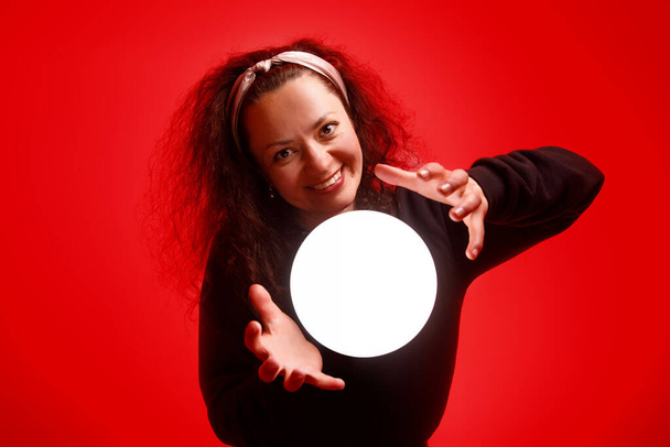 Chica sonriente sosteniendo una bola brillante en sus manos Fondo rojo
 - Foto, Imagen