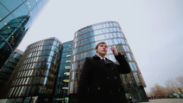 A male businessman in a black coat is talking on the phone in the street at a business center. - Séquence, vidéo