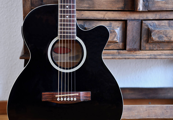 Black acoustic guitar in front of vintage wooden cupboard. - Photo, Image