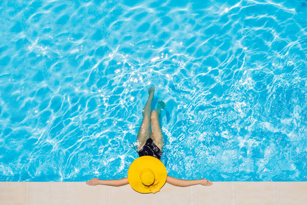 Woman sitting in a swimming pool in a large yellow sunhat - Foto, afbeelding