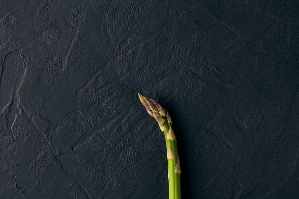 Un tallo de espárragos verdes frescos crudos sobre fondo de pizarra negra. Concepto de cultivo de alimentos y verduras de temporada. Cerrar, copiar espacio
 - Foto, imagen