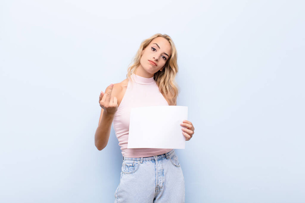 young blonde woman feeling angry, annoyed, rebellious and aggressive, flipping the middle finger, fighting back holding a sheet of paper - Φωτογραφία, εικόνα
