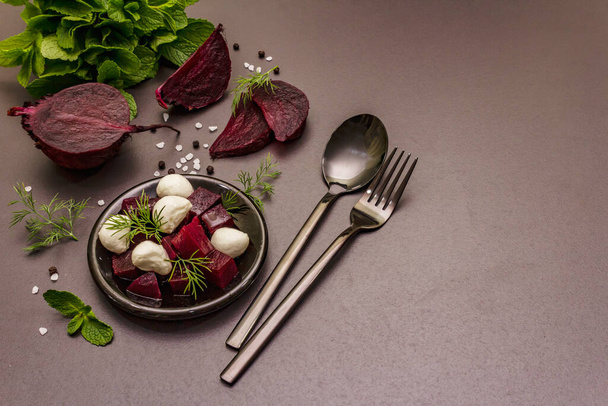 Culinary background. Cooking food concept. Healthy salad with baked beetroot, baby mozzarella, fresh greens. Trendy black stone concrete backdrop, copy space - Photo, Image