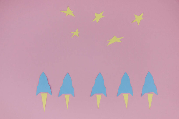 Una fila de cohetes espaciales de papel volando hacia las estrellas sobre una superficie de papel rosa. Concepto espacial. Copiar espacio
. - Foto, imagen