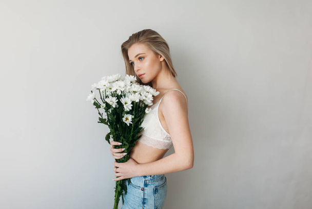 A beautiful girl with blonde hair in underwear is holding a bouquet of daisies. Blonde and a bunch of daisies for mother's Day - Фото, зображення
