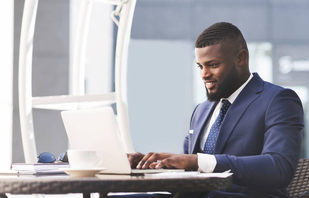 Успішний чорний бізнесмен працює на ноутбуці онлайн сидячи в кафе
 - Фото, зображення