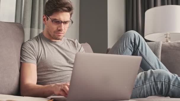 Young serious man indoors at home using laptop computer - Filmagem, Vídeo