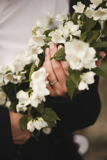 A girl in a white shirt holds a bouquet of flowers, an engagement ring on her hand, closeup photo. French manicure on hand - Fotoğraf, Görsel