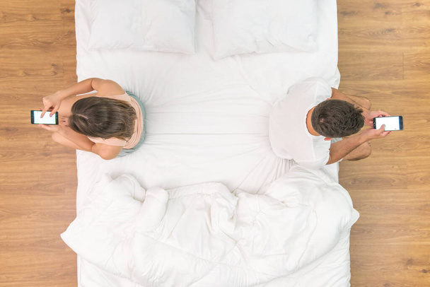 The man and woman with phone sit on the bed. view from above - Foto, Imagen