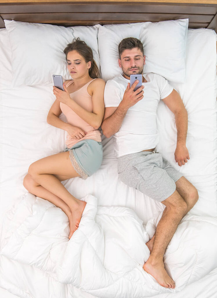 The young couple lay on the bed and phone. View from above - Photo, Image
