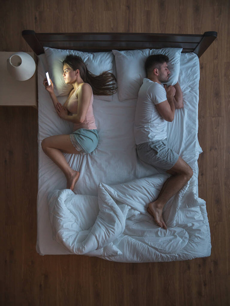 De vrouw met telefoon lag op het bed naast haar man. zicht van bovenaf - Foto, afbeelding