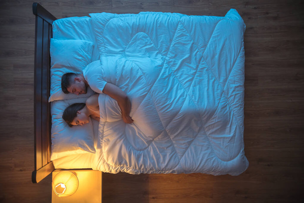Чоловік обіймає жінку на ліжку. нічний час. вид зверху
 - Фото, зображення