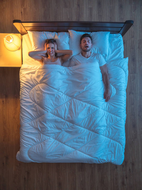 El hombre ronca cerca de la esposa en la cama. noche de noche. vista desde arriba
 - Foto, Imagen