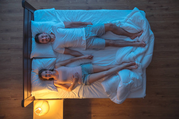 Щаслива пара тримає руки на ліжку. вечірній нічний час. вид зверху
 - Фото, зображення