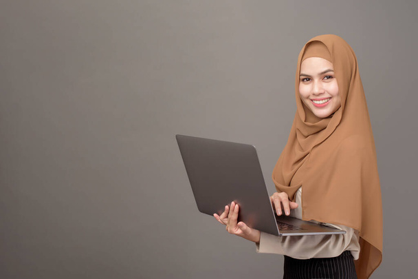 Portrait of beautiful woman with hijab is holding computer laptop on gray background  - Foto, imagen