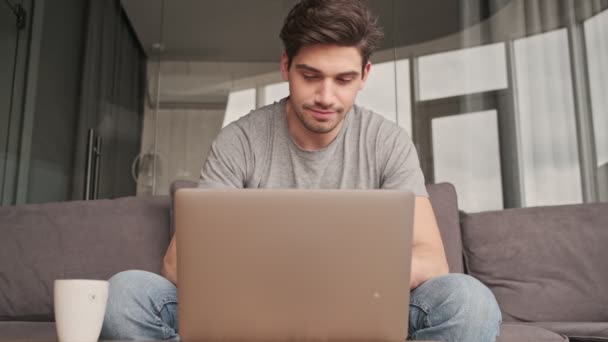Όμορφος νεαρός άνδρας σε εσωτερικούς χώρους στο σπίτι χρησιμοποιώντας φορητό υπολογιστή - Πλάνα, βίντεο