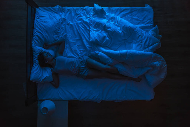 The woman sleeping on the bed. Evening night time. View from above - Фото, изображение