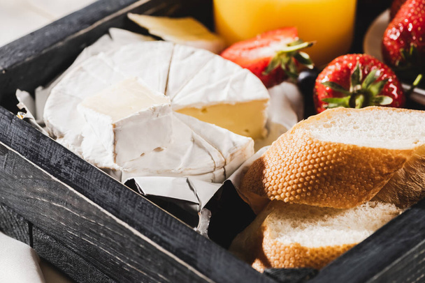 close up view of french breakfast with Camembert, strawberries and baguette on wooden tray - Photo, Image