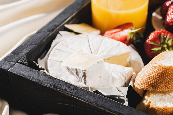 close up άποψη του γαλλικού πρωινού με Camembert, χυμό πορτοκαλιού, φράουλες και μπαγκέτα σε ξύλινο δίσκο - Φωτογραφία, εικόνα