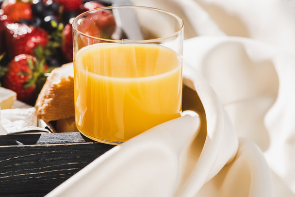 close up view of french breakfast with orange juice, berries on wooden tray on textured white cloth - Photo, Image