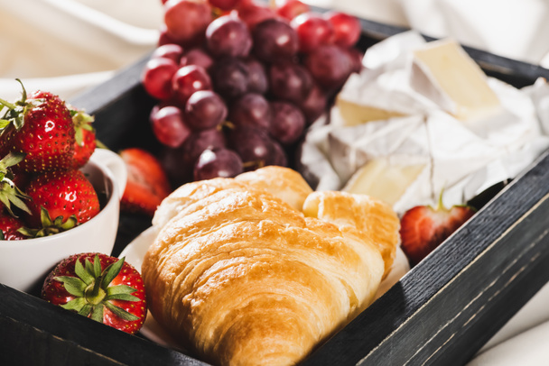 close up view of french breakfast with croissant, Camembert, grape, strawberries on wooden tray on textured white cloth - Photo, Image