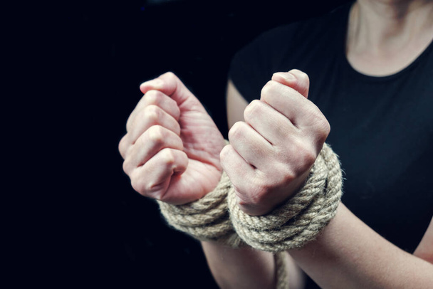 Manos de una mujer víctima atadas con una cuerda áspera en el fondo negro. Deja de abusar del concepto de violencia - Foto, imagen