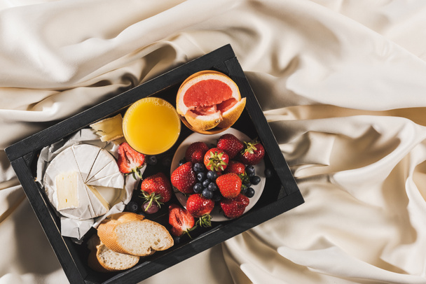 top view of french breakfast with grapefruit, Camembert, orange juice, berries and baguette on tray on white tablecloth - Photo, Image
