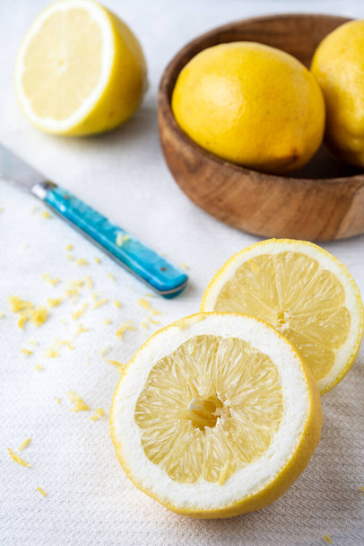 Close-up of half lemons, lemon zest, blue knife and wooden bowl with lemons, on white dishcloth, selective focus, vertical - Foto, Imagem