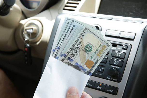 Dólares en efectivo en un sobre en el fondo del interior de un coche. Concepto de venta, compra y arrendamiento de coches
. - Foto, Imagen